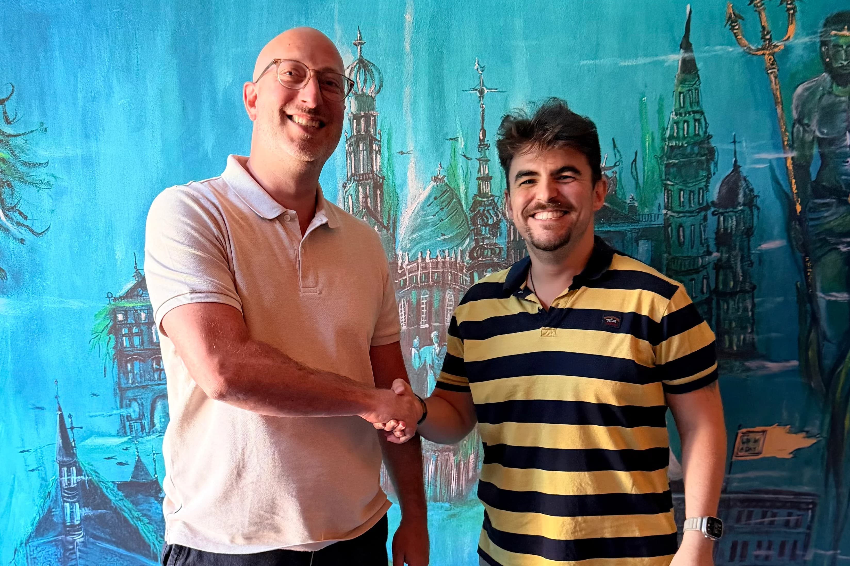 Necati Atakan Alevli shaking hands with a client in front of a hand-painted mural of an underwater city.