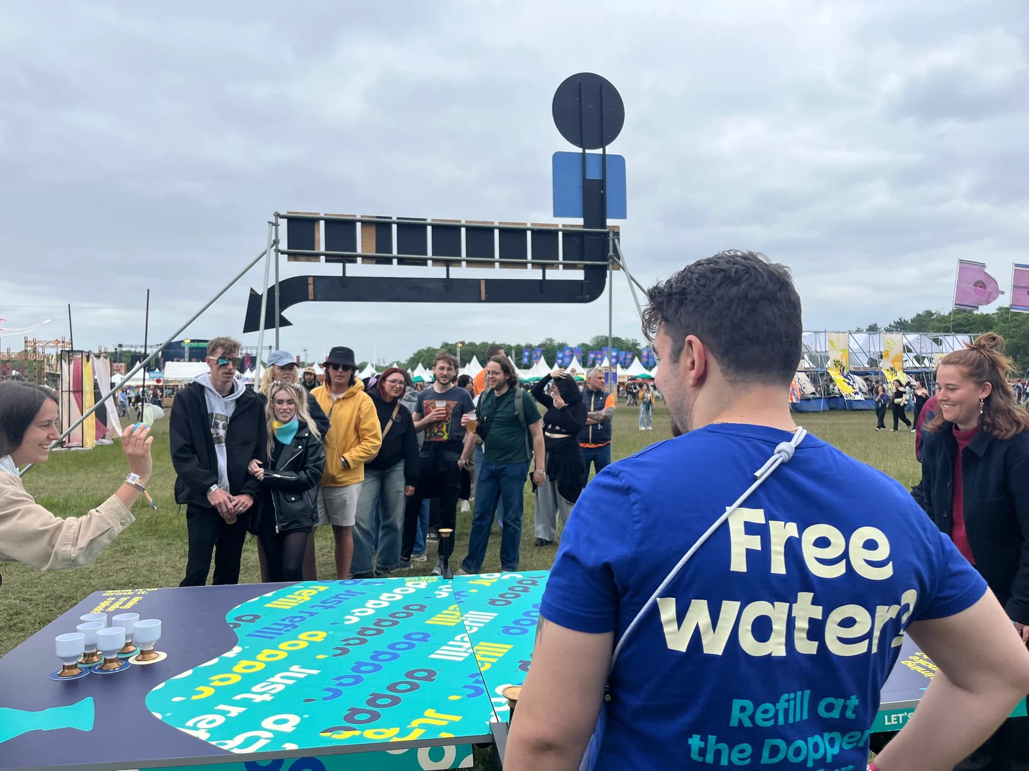 Festival visitors queuing at the Dopper Water Pong table waiting their turn to play, while a player takes a shot at the cups.